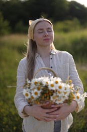 Photo of Happy woman with basket full of beautiful wildflowers outdoors