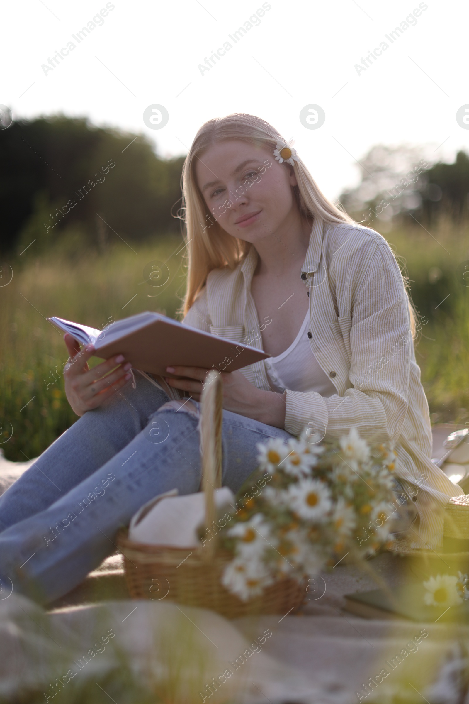 Beautiful woman with bouquet of wildflowers reading book on blanket in meadow Photo of Beautiful woman with bouquet of wildflowers reading book on blanket in meadow