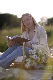 Photo of Beautiful woman with bouquet of wildflowers reading book on blanket in meadow