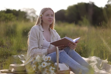 Photo of Beautiful woman with bouquet of wildflowers reading book on blanket in meadow