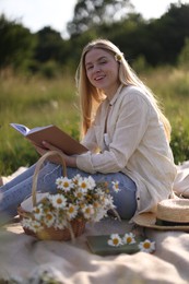 Photo of Beautiful woman with bouquet of wildflowers reading book on blanket in meadow