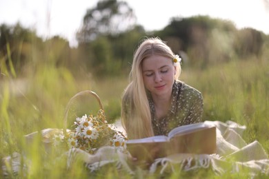 Photo of Beautiful woman with bouquet of wildflowers reading book on blanket in meadow