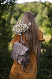 Photo of Beautiful woman with bouquet of wildflowers and backpack in forest, back view