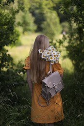 Photo of Beautiful woman with bouquet of wildflowers and backpack in forest, back view
