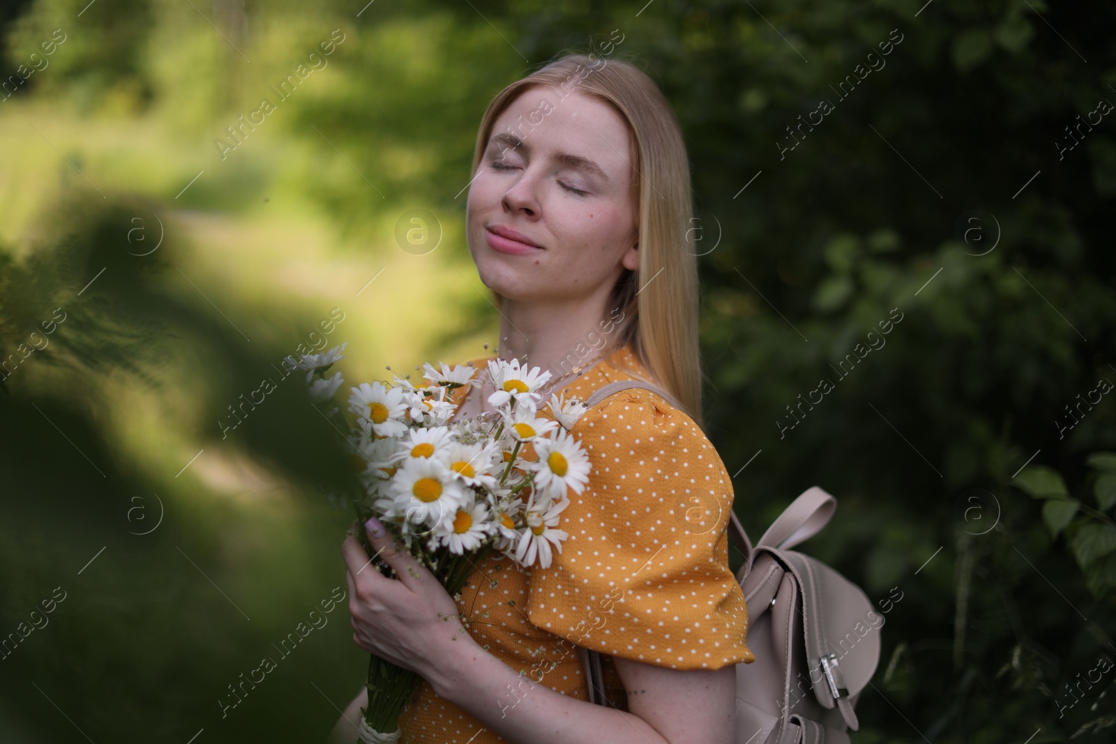 Beautiful woman with bouquet of wildflowers and backpack in forest Photo of Beautiful woman with bouquet of wildflowers and backpack in forest