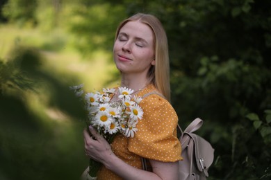 Photo of Beautiful woman with bouquet of wildflowers and backpack in forest