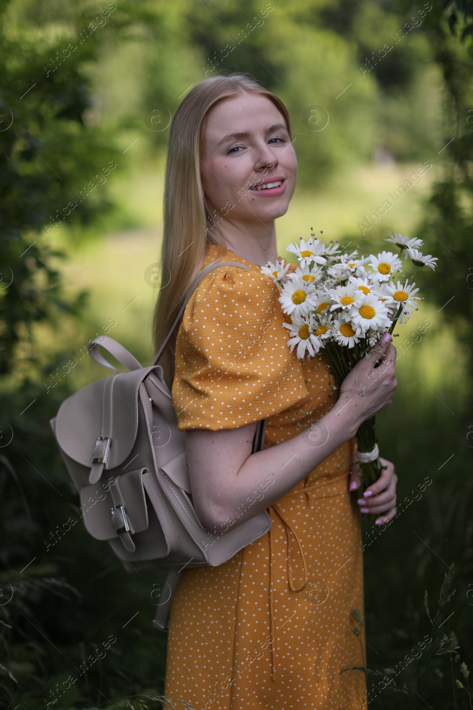 Beautiful woman with bouquet of wildflowers and backpack in forest Photo of Beautiful woman with bouquet of wildflowers and backpack in forest