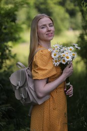 Photo of Beautiful woman with bouquet of wildflowers and backpack in forest