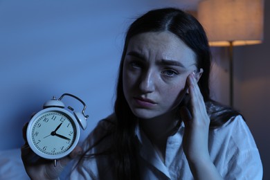 Photo of Frustrated woman with alarm clock suffering from insomnia indoors