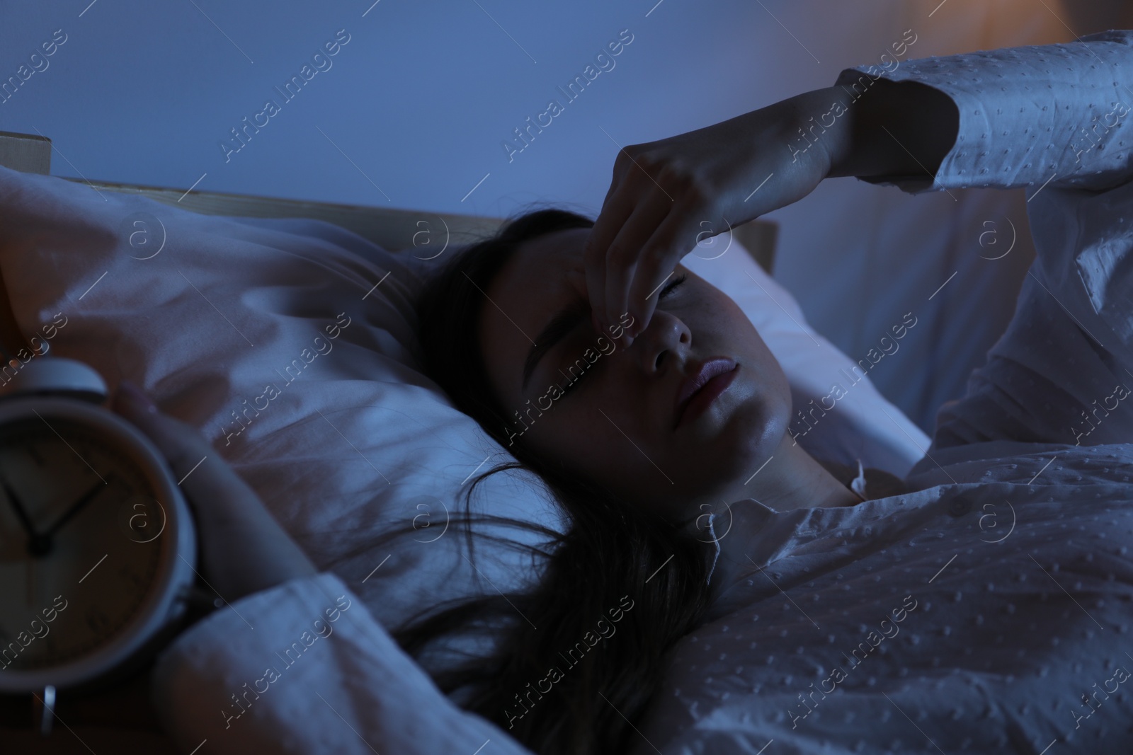 Frustrated woman with alarm clock suffering from insomnia in bed at home Photo of Frustrated woman with alarm clock suffering from insomnia in bed at home