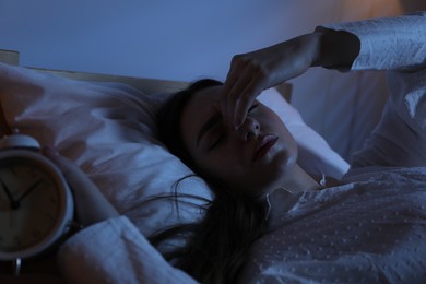 Photo of Frustrated woman with alarm clock suffering from insomnia in bed at home