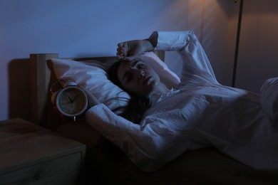 Photo of Frustrated woman with alarm clock suffering from insomnia in bed at home