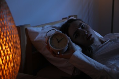 Photo of Frustrated woman with alarm clock suffering from insomnia in bed at home