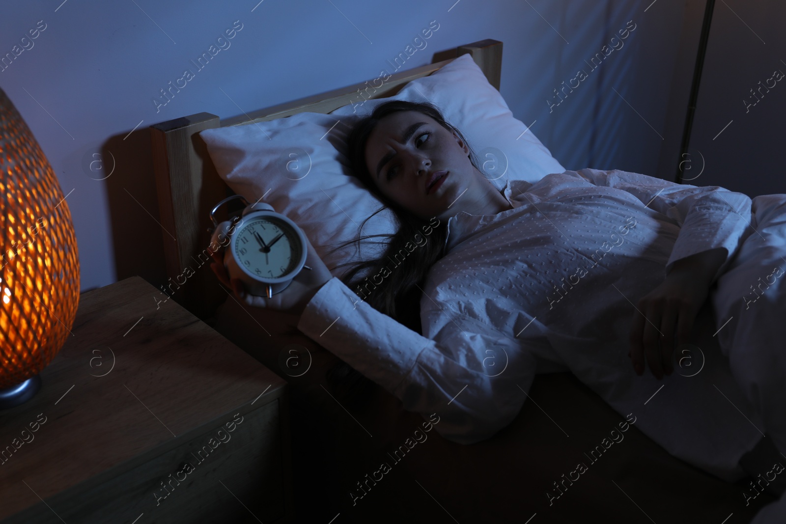 Photo of Frustrated woman with alarm clock suffering from insomnia in bed at home