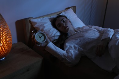 Photo of Frustrated woman with alarm clock suffering from insomnia in bed at home