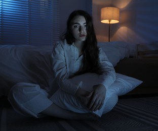Photo of Frustrated woman with pillow suffering from insomnia on floor at home