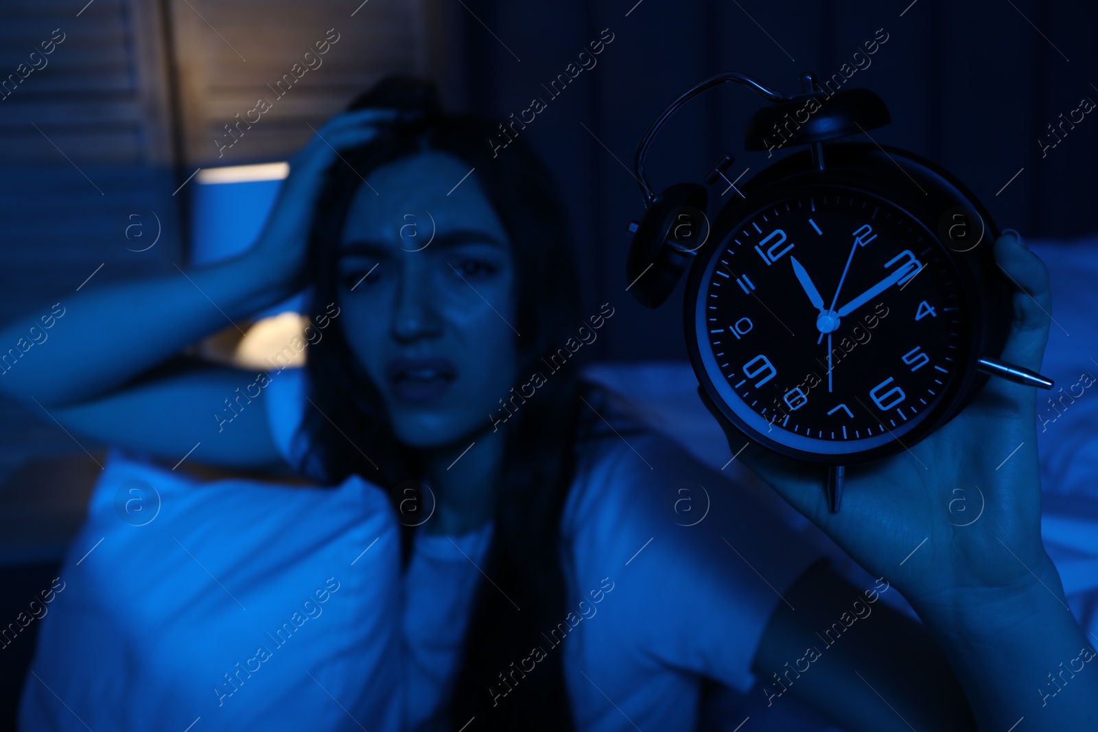 Photo of Frustrated woman with pillow and alarm clock suffering from insomnia at home, selective focus