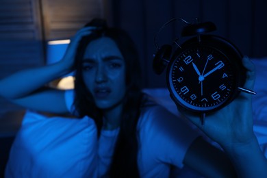 Photo of Frustrated woman with pillow and alarm clock suffering from insomnia at home, selective focus