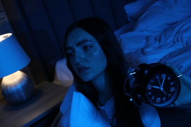 Photo of Frustrated woman with pillow and alarm clock suffering from insomnia at home