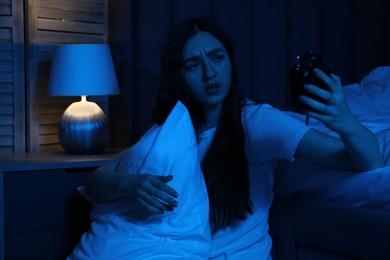Photo of Frustrated woman with pillow and alarm clock suffering from insomnia on floor at home