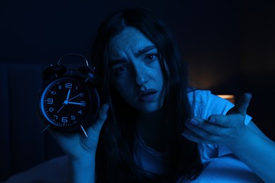 Photo of Frustrated woman with alarm clock suffering from insomnia on bed at home