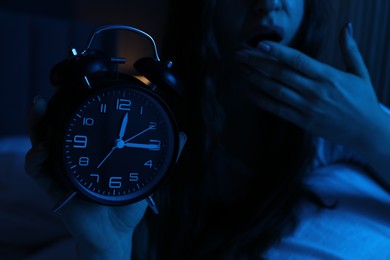 Photo of Frustrated woman with alarm clock suffering from insomnia on bed at home, closeup