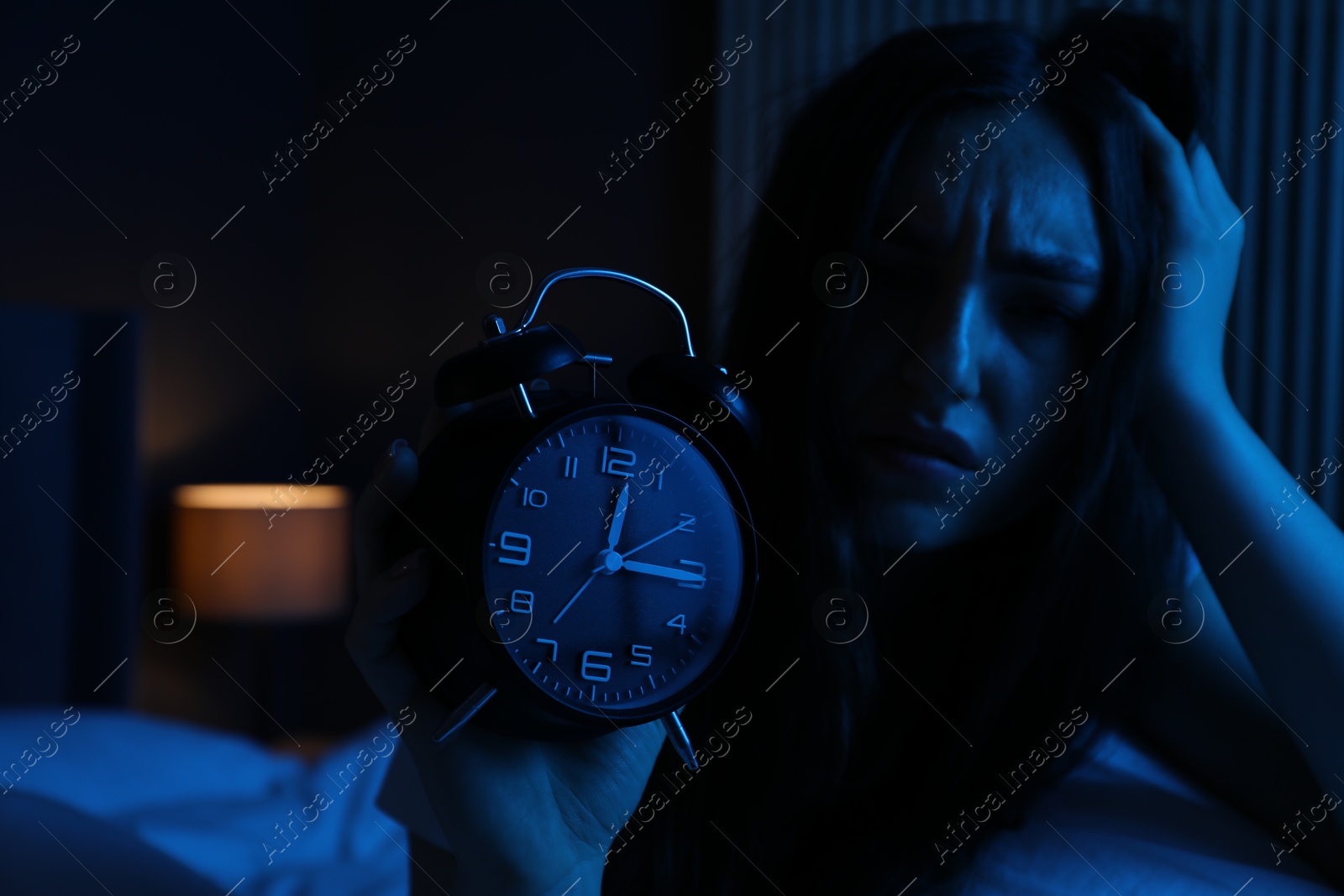 Frustrated woman with alarm clock suffering from insomnia on bed at home Photo of Frustrated woman with alarm clock suffering from insomnia on bed at home