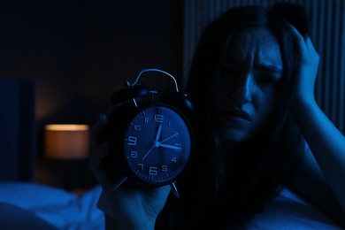Photo of Frustrated woman with alarm clock suffering from insomnia on bed at home