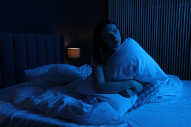 Photo of Frustrated woman with pillow suffering from insomnia on bed at home