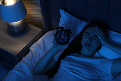 Photo of Frustrated woman with alarm clock suffering from insomnia in bed at home, above view