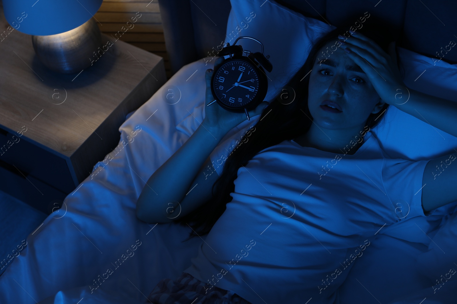 Frustrated woman with alarm clock suffering from insomnia in bed at home, above view Photo of Frustrated woman with alarm clock suffering from insomnia in bed at home, above view