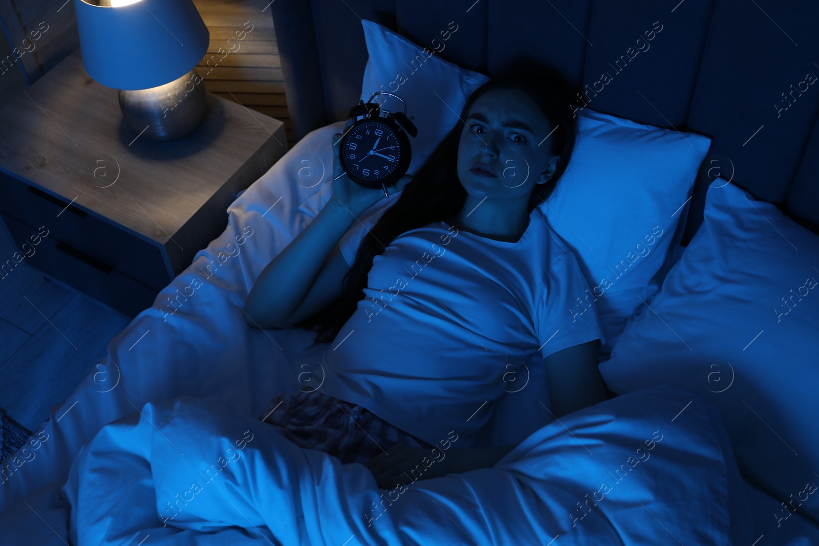 Frustrated woman with alarm clock suffering from insomnia in bed at home, above view Photo of Frustrated woman with alarm clock suffering from insomnia in bed at home, above view