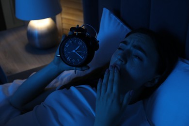 Photo of Frustrated woman with alarm clock suffering from insomnia in bed at home