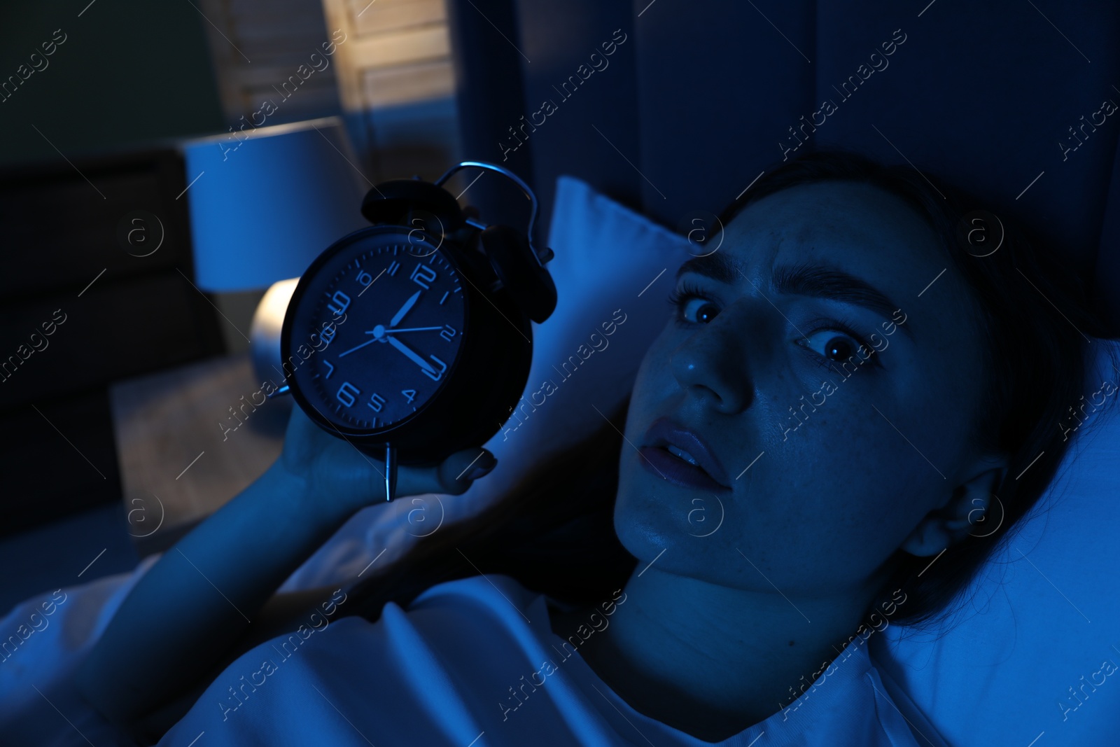 Frustrated woman with alarm clock suffering from insomnia in bed at home Photo of Frustrated woman with alarm clock suffering from insomnia in bed at home