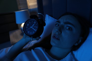 Photo of Frustrated woman with alarm clock suffering from insomnia in bed at home