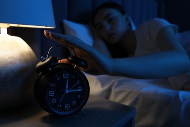 Photo of Frustrated woman suffering from insomnia and turning off alarm clock in bed indoors, selective focus