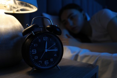 Photo of Frustrated woman suffering from insomnia in bed at home, focus on alarm clock