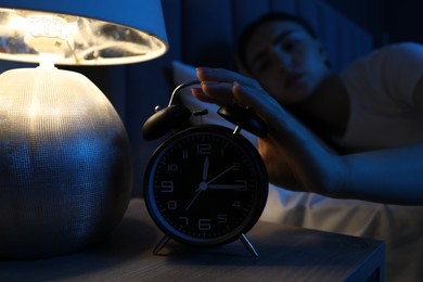 Photo of Frustrated woman suffering from insomnia and turning off alarm clock in bed indoors, selective focus