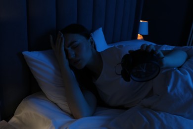 Photo of Frustrated woman with alarm clock suffering from insomnia in bed at home