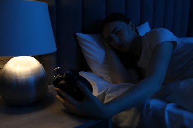 Photo of Frustrated woman with alarm clock suffering from insomnia in bed at home