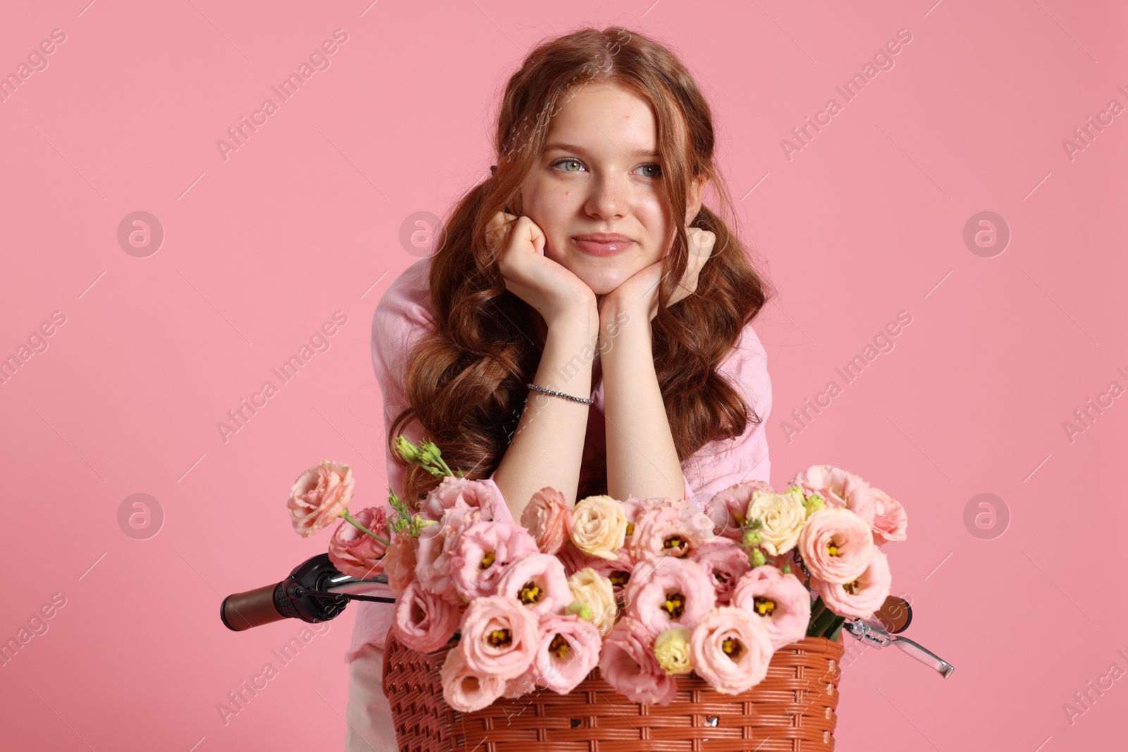Photo of Beautiful teenage girl posing on bicycle with basket of flowers against pink background