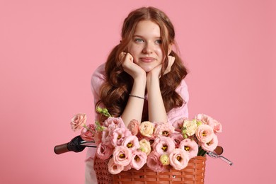 Photo of Beautiful teenage girl posing on bicycle with basket of flowers against pink background