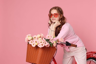 Photo of Beautiful teenage girl in sunglasses and bicycle with basket of flowers against pink background. Space for text