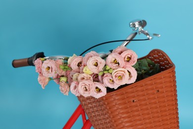 Photo of Bicycle with wicker basket of beautiful flowers on light blue background, closeup