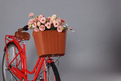 Photo of Bicycle with basket of beautiful flowers on grey background, closeup. Space for text