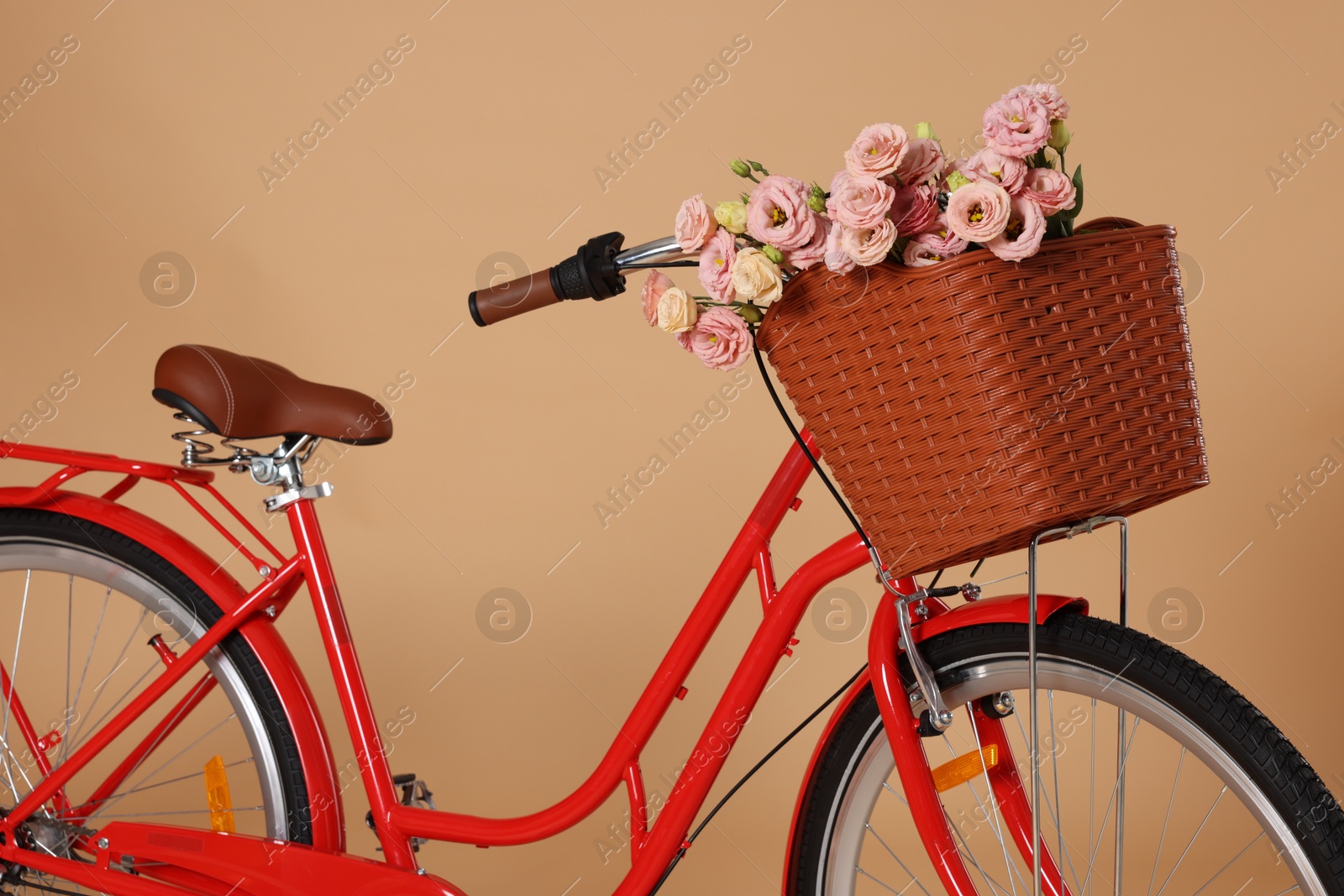 Bicycle with basket of beautiful flowers on pale orange background, closeup Photo of Bicycle with basket of beautiful flowers on pale orange background, closeup