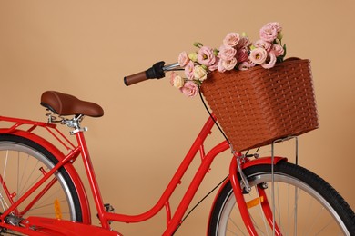 Photo of Bicycle with basket of beautiful flowers on pale orange background, closeup