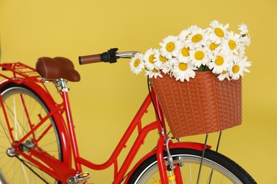 Photo of Bicycle with basket of beautiful flowers on yellow background, closeup