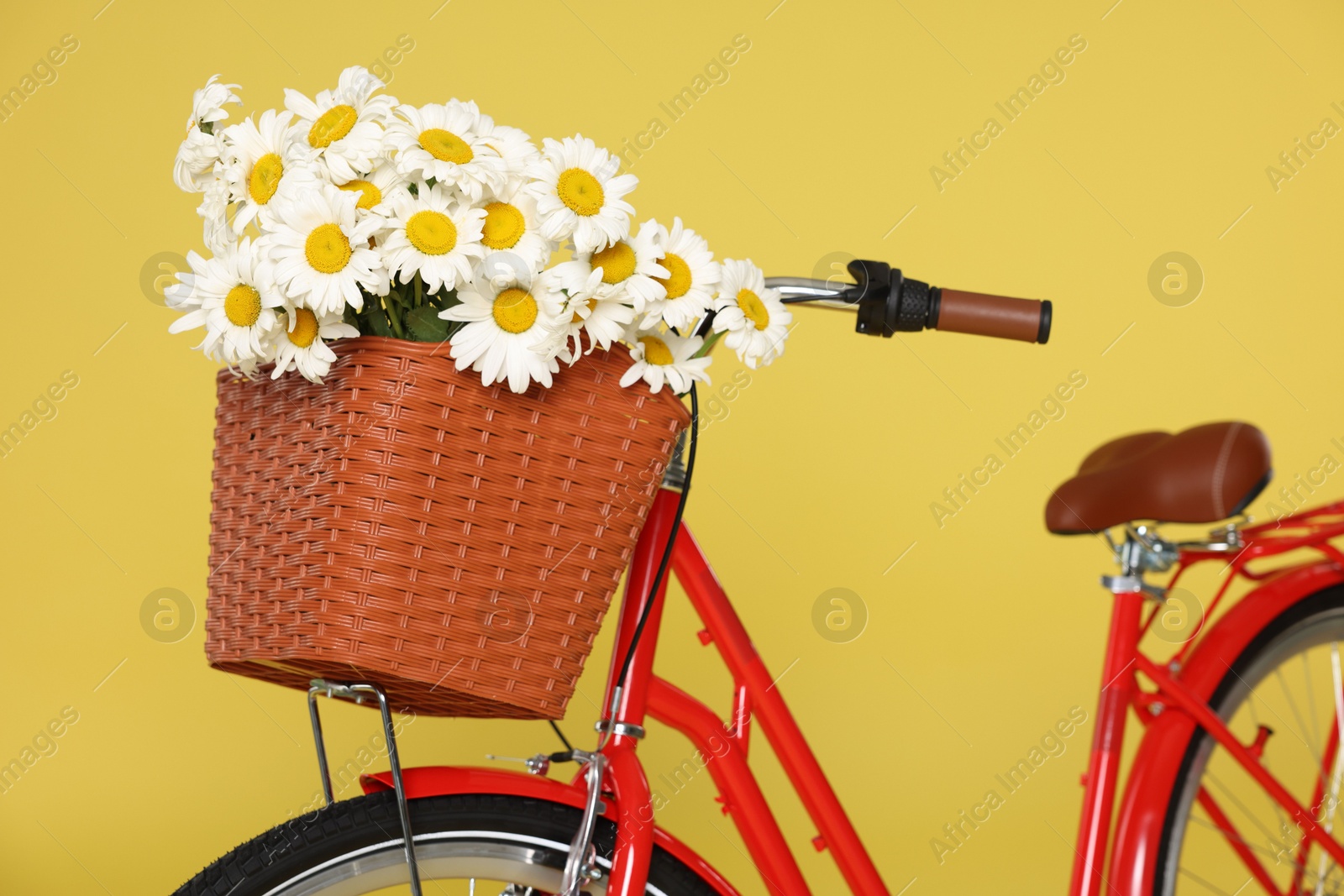 Bicycle with basket of beautiful flowers on yellow background, closeup Photo of Bicycle with basket of beautiful flowers on yellow background, closeup