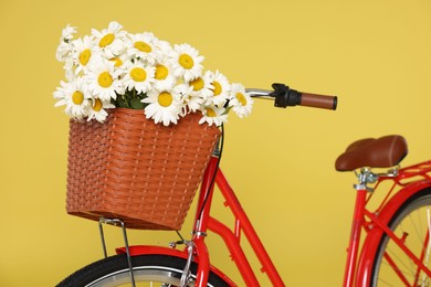 Photo of Bicycle with basket of beautiful flowers on yellow background, closeup